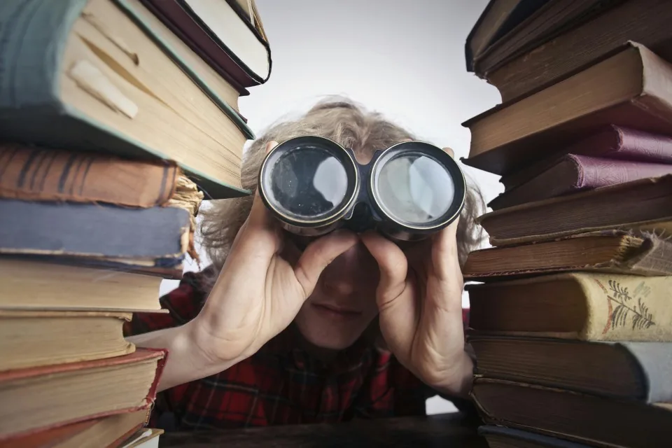 picture of a man peering through binoculars between two stacks of books
